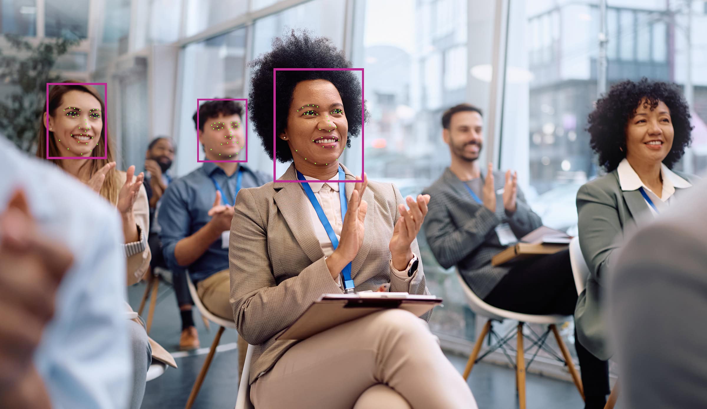 A diverse group of people in a modern conference room applauding. They are smiling, showing engagement and positivity, with large windows in the background.